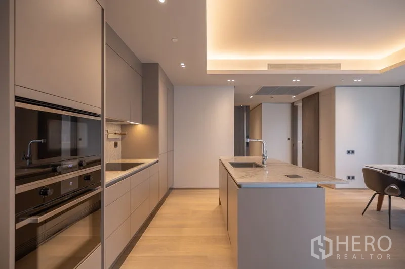 Condominium for rent in Pathum Wan, Bangkok - Galley kitchen with premium appliances, marble island and warm ambient lighting.