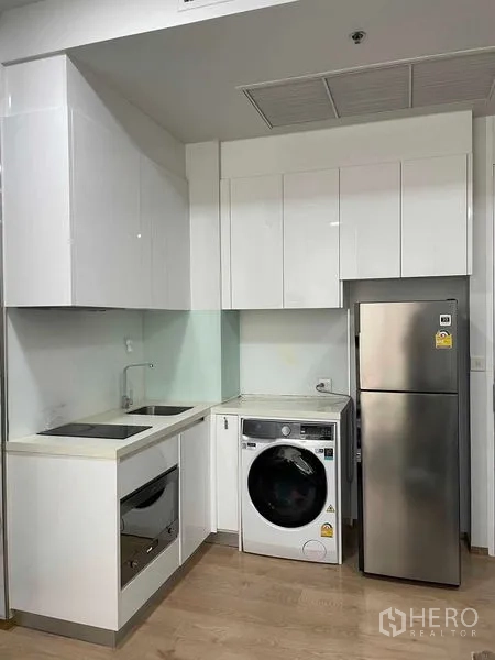 Condominium for rent in Watthana, Bangkok - Compact white kitchen with electric cooktop, oven, sink and washer-dryer.