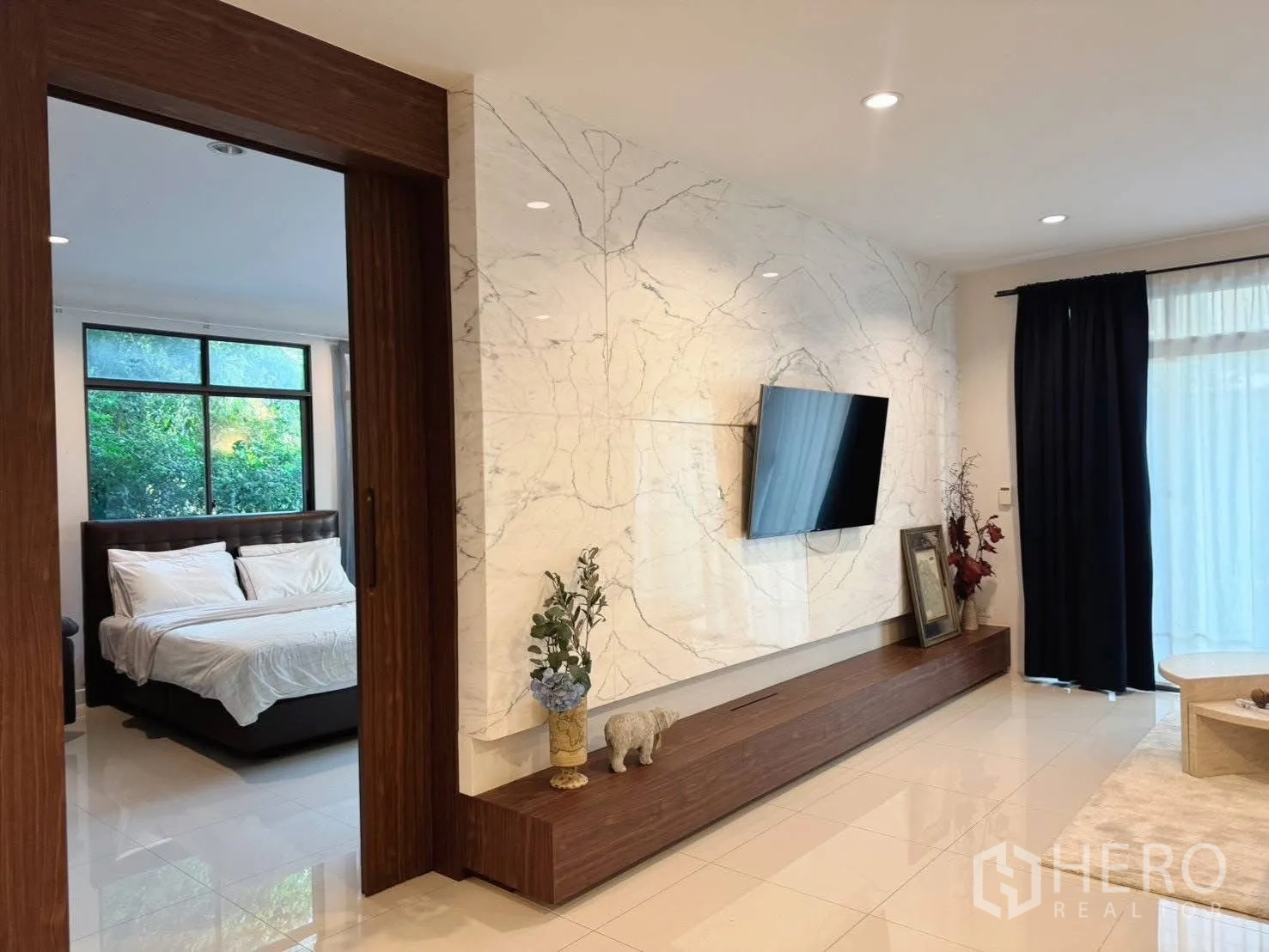 บ้านเดี่ยว for rent or sale in Suan Luang, Bangkok - ห้องนั่งเล่นผนังลายหินอ่อนติดทีวี มองทะลุประตูไม้เข้าสู่ห้องนอน