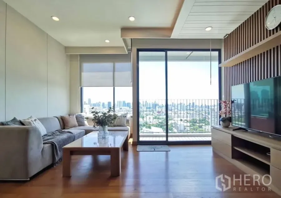 Condominium for rent in Sathon, Bangkok - Bright living room with L-shaped sofa, TV wall and balcony overlooking the Bangkok skyline.