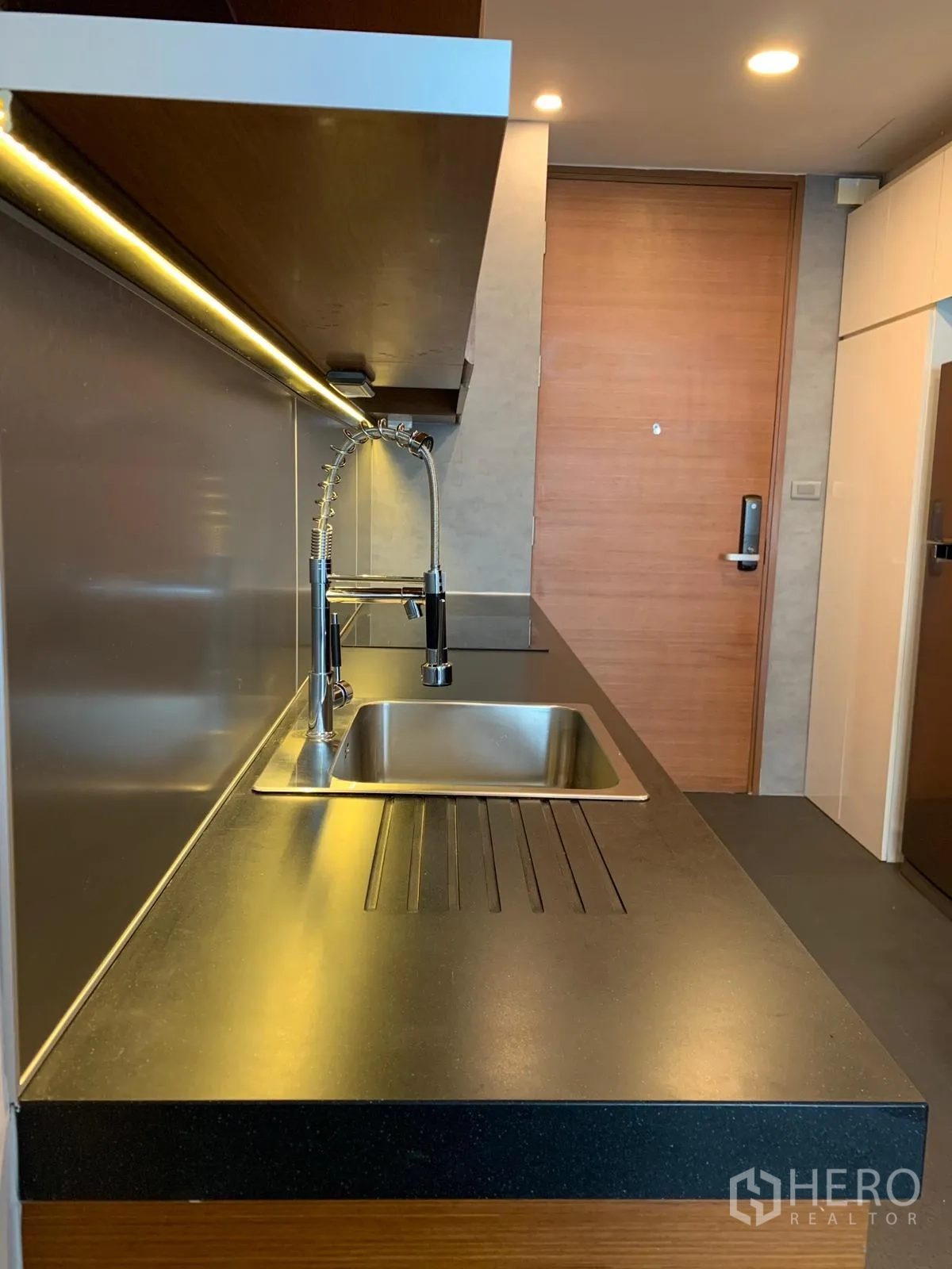 Condominium for sale in Khlong Toei, Bangkok - Kitchen worktop and sink with under‑cabinet lighting near the entrance door.