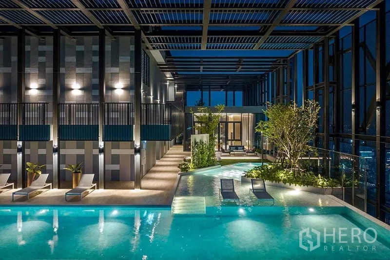 Condominium for rent in Ratchathewi, Bangkok - Rooftop swimming pool with loungers, greenery and ambient night lighting.