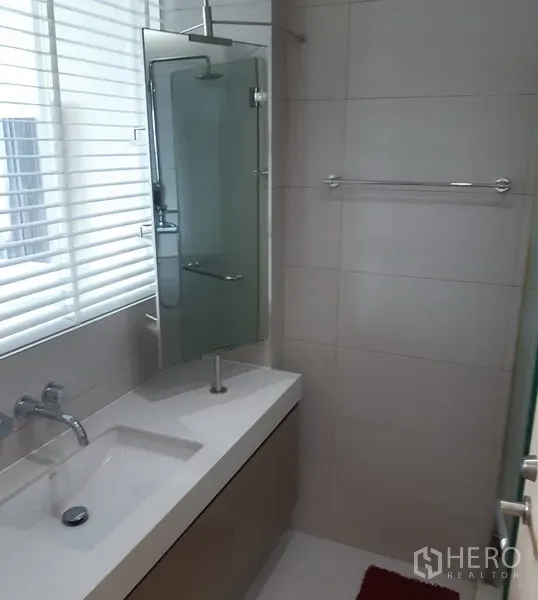 Condominium for rent in Khlong Toei, Bangkok - Contemporary bathroom with vanity, glass shower screen and window with blinds.