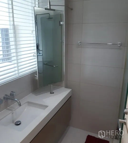Condominium for rent in Khlong Toei, Bangkok - Contemporary bathroom with vanity, glass shower screen and window with blinds.