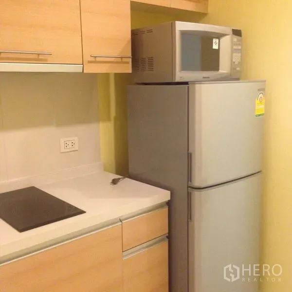 Condominium for rent in Khlong Toei, Bangkok - Compact kitchen with light-wood cabinets, electric cooktop, microwave and full-size refrigerator.