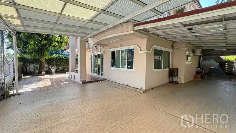 独立式住宅 出售在Mueang Pathum Thani, Pathum Thani - 两层独栋别墅的前庭与有顶车棚，铺装车道与绿化。