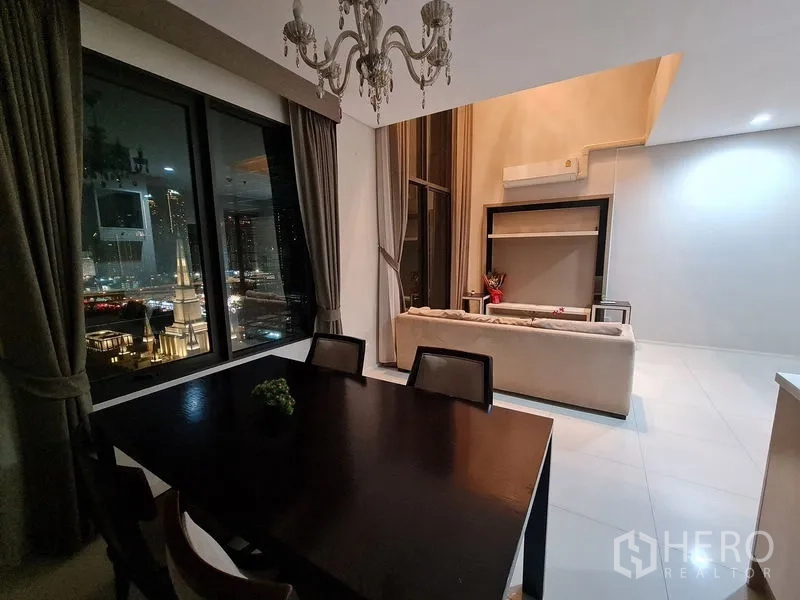 公寓 出售在Ratchathewi, Bangkok - 餐桌与吊灯俯瞰客厅，双层挑高落地窗的夜景