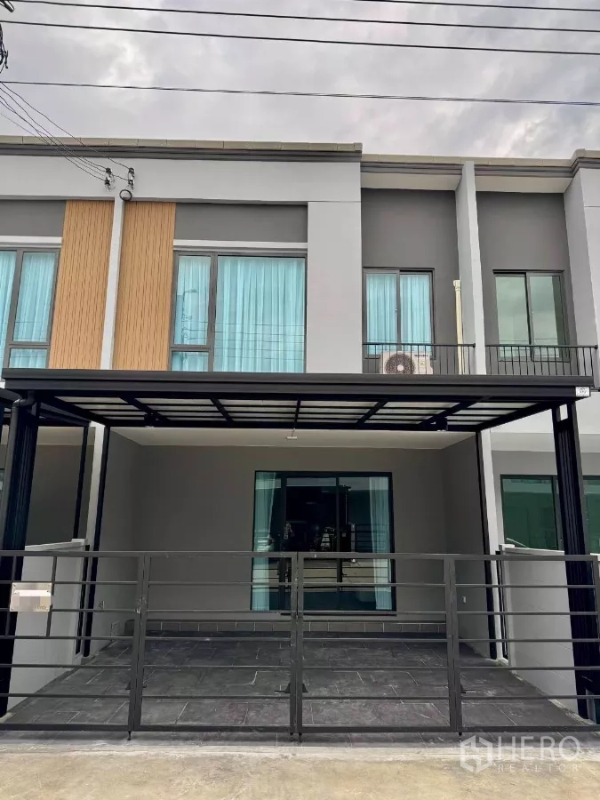 Townhouse for rent in Bang Phli, Samut Prakan - Modern two-storey townhouse facade with covered carport and blue curtains