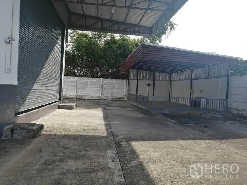 Warehouse for rent in Lat Krabang, Bangkok - Side yard with a roller shutter door and a covered service shelter behind a secure perimeter wall.