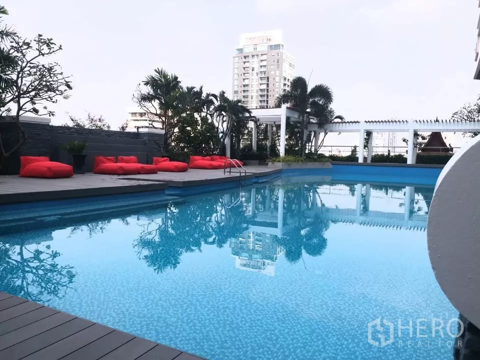 Condominium for rent in Khlong Toei, Bangkok - Resort-style pool with red bean bag loungers and a shaded pavilion amid city towers.