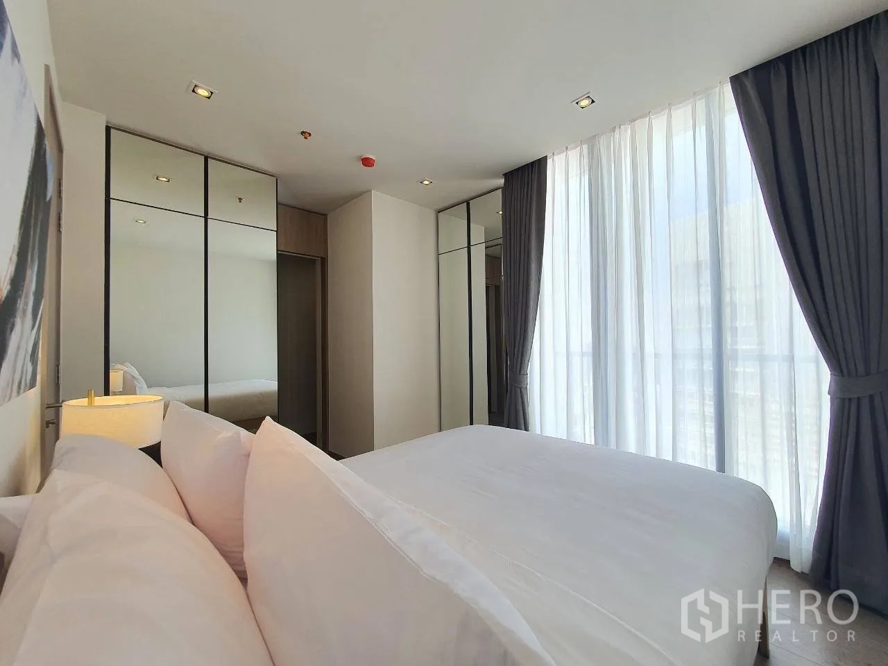 Condominium for rent in Khlong Toei, Bangkok - Bright bedroom with floor-to-ceiling windows, blackout curtains, and mirrored wardrobes.