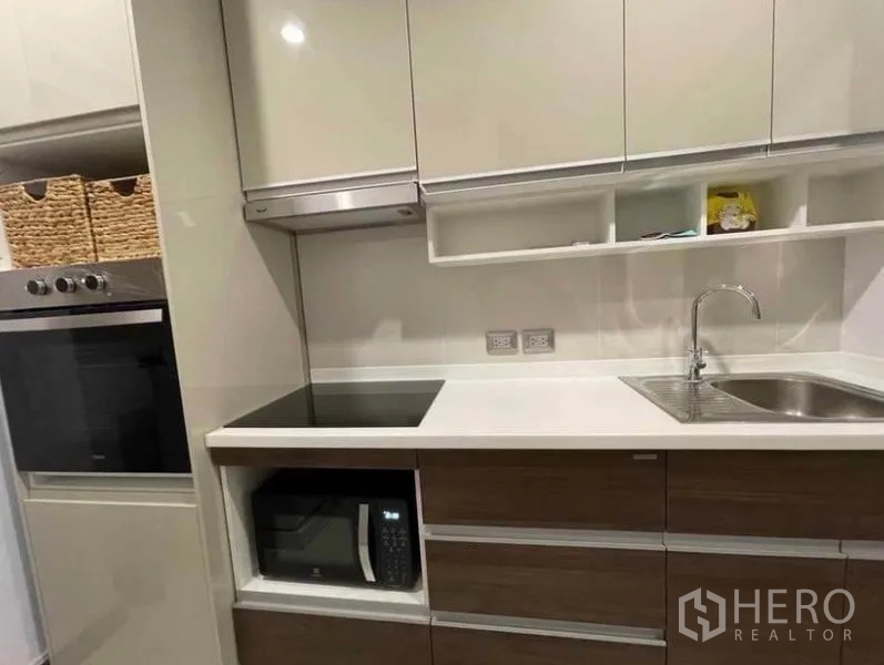 Condominium for rent in Watthana, Bangkok - Modern kitchen counter with electric hob, oven, microwave and stainless sink.