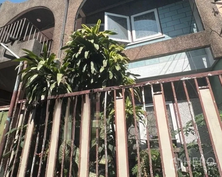 Townhouse for sale - Two-storey Ekkamai townhouse facade with arched balcony, open windows, and mature greenery behind a metal gate.