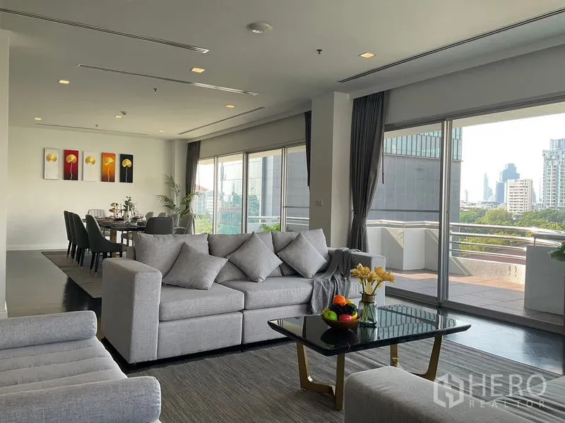 Apartment for rent in Sathon, Bangkok - Open‑plan living and dining area with wall‑to‑wall glass and balcony access.