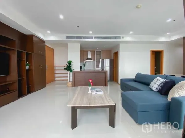 公寓 出租或出售在Bangkok - 开放式客厅，蓝色转角沙发、厨房岛台与内置电视柜。