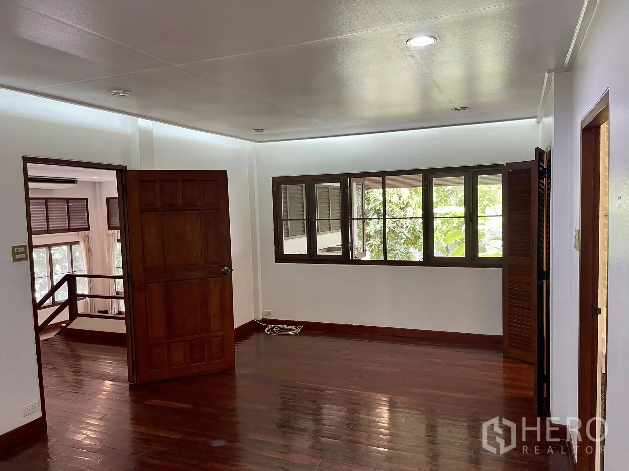 Detached House for rent in Pathum Wan, Bangkok - Bright room with polished wooden floors, wood doors, and windows overlooking greenery.
