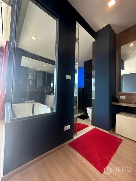 Condominium for sale in Phaya Thai, Bangkok - Modern bathroom corridor with glass wall shower, vanity, and red rugs.