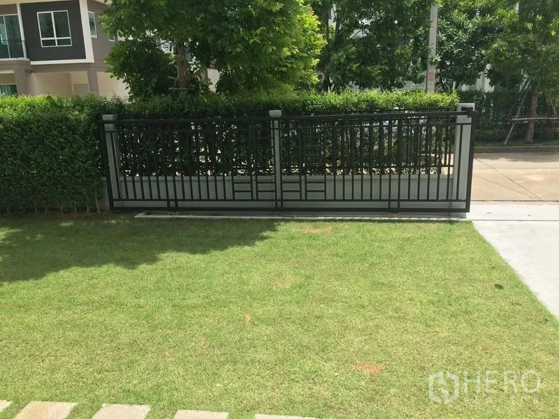 Detached House for rent in Khlong Luang, Pathum Thani - Front lawn with metal fence and manicured hedges along the boundary.