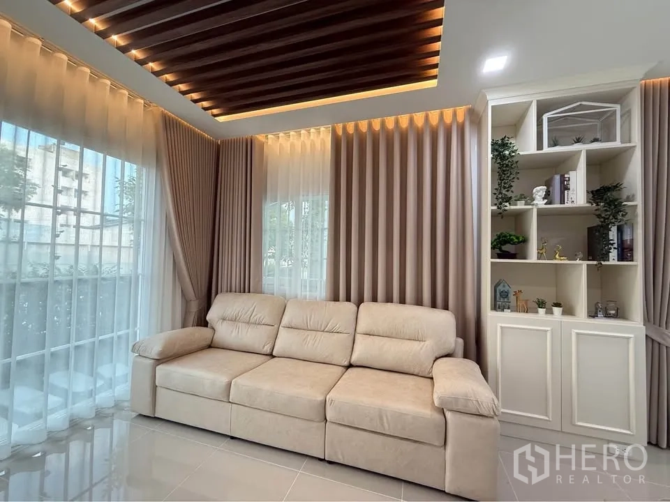 Semi-detached House for rent in Mueang Samut Prakan, Samut Prakan - Living room corner with beige sofa, large windows, and built-in shelving.