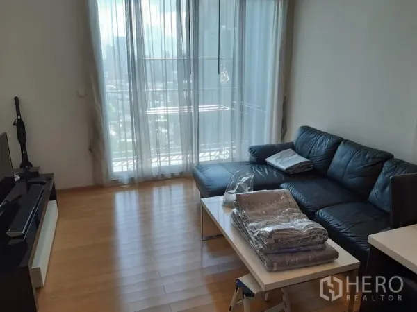 Condominium for rent in Khlong Toei, Bangkok - Bright living room with leather sofa, TV console, and floor-to-ceiling balcony windows.