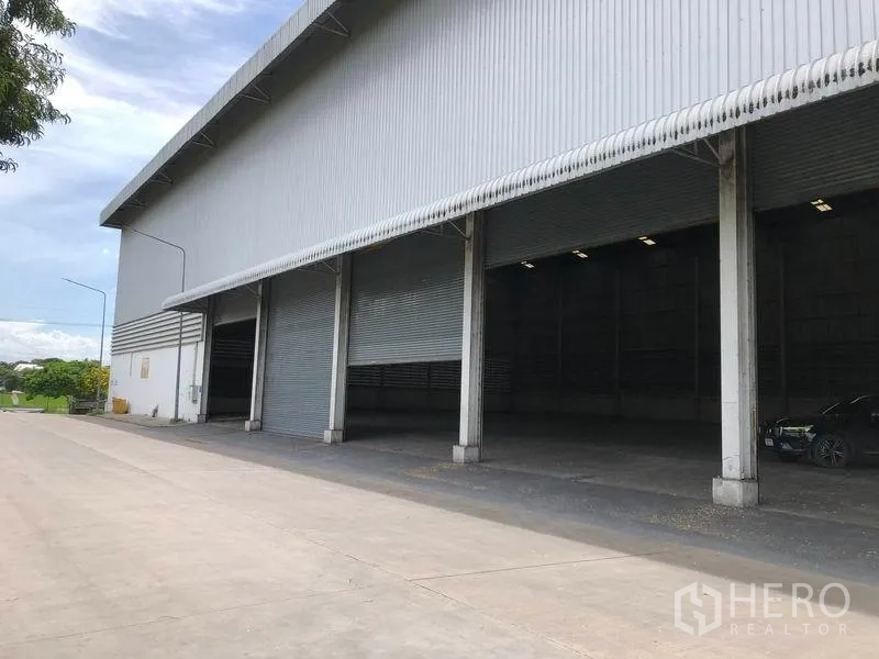 Warehouse for rent in Phra Nakhon Si Ayutthaya - Multiple roller shutters and a sheltered loading area on a concrete apron beside the warehouse.