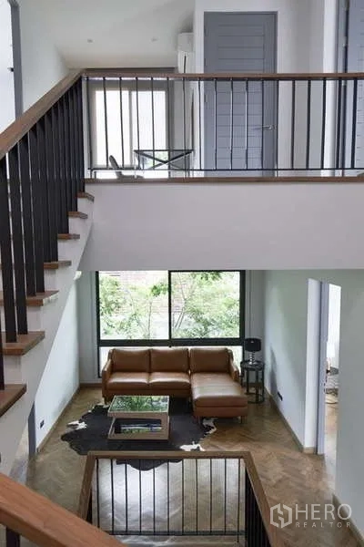 Townhouse for sale in Watthana, Bangkok - Double-height living room with mezzanine railing and a large window facing greenery.