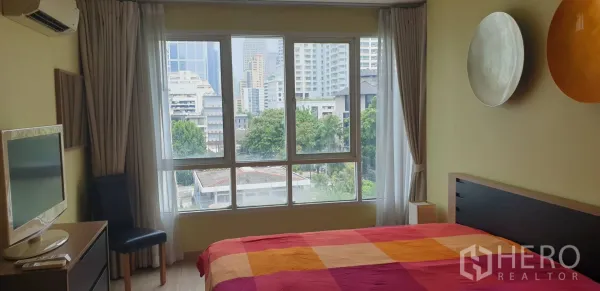 公寓 出租在Khlong Toei, Bangkok - 采光充足的卧室，落地窗享城市景观，彩色床品。