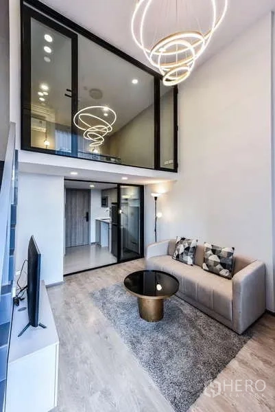 Condominium for rent in Huai Khwang, Bangkok - Loft-style living room with double-height ceiling and sculptural chandelier.