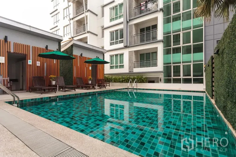 Condominium for rent in Khlong Toei, Bangkok - Outdoor condominium swimming pool with sun loungers, umbrellas, and the building facade.