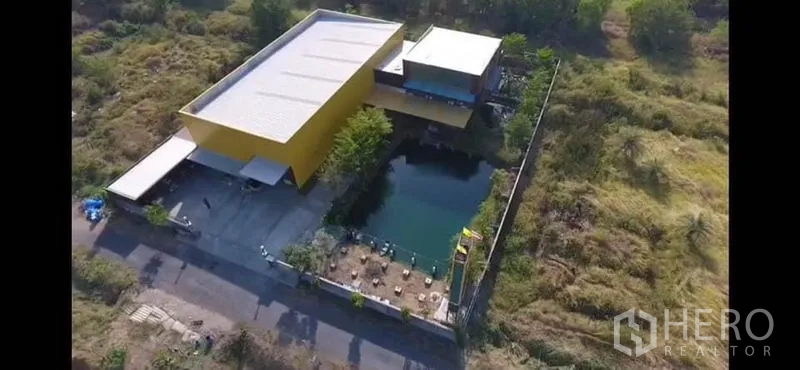 工厂 出售在Thanyaburi, Pathum Thani - 俯瞰工厂园区，可见仓库、停车装卸区及围墙内的大型水塘。