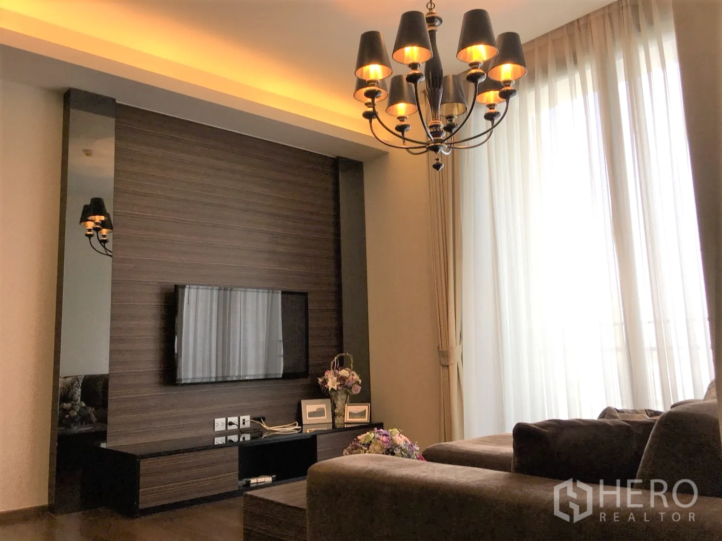 公寓 出租在Watthana, Bangkok - 客厅配电视背景墙、转角沙发与暖色灯光。