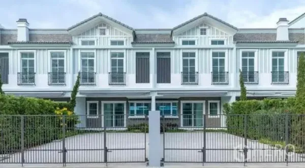 联排别墅 出租在Prawet, Bangkok - 两层现代白色联排别墅外立面，带围栏车道与修剪整齐的绿篱。