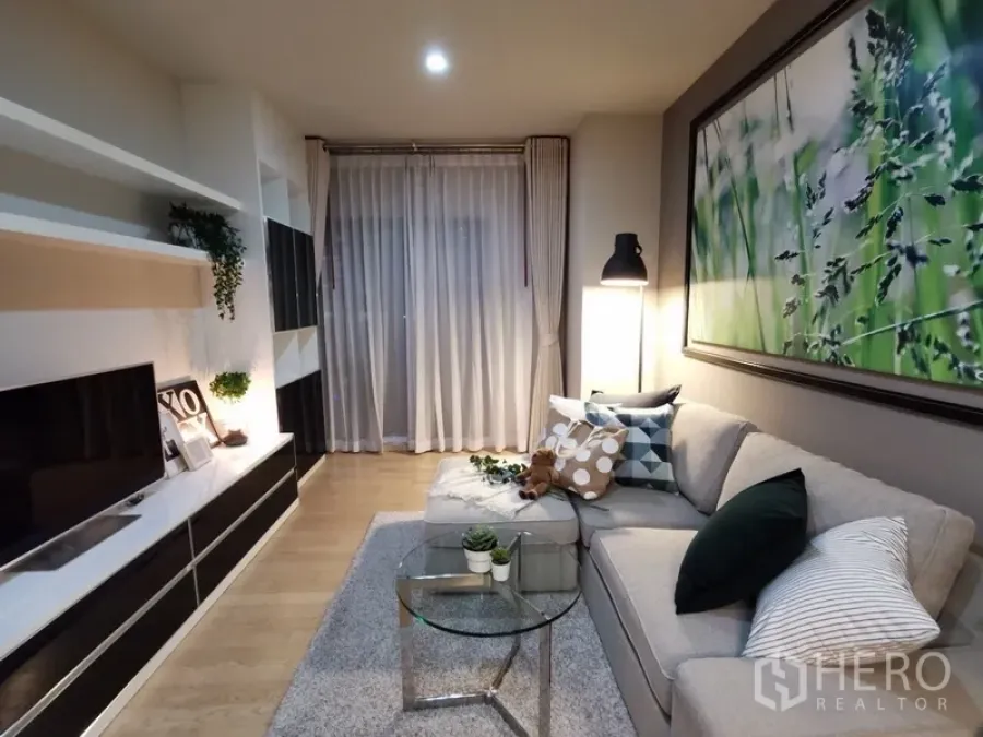 คอนโด ขายในBangkok - ห้องนั่งเล่นอบอุ่น โซฟาเข้ามุม ชั้นวางทีวีบิวท์อิน ผ้าม่านโปร่ง และไฟสลัวนุ่มนวล
