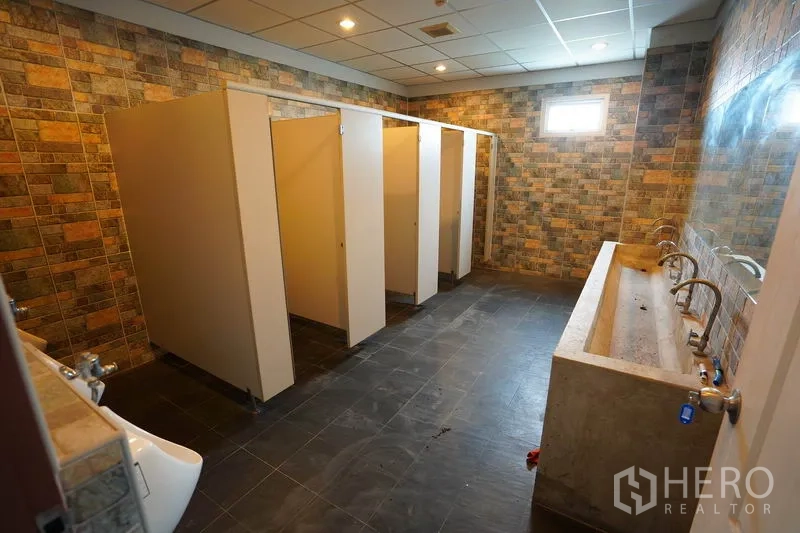 Factory for sale in Khlong Luang, Pathum Thani - Restroom block with multiple stalls, stone-pattern walls and long concrete sink.
