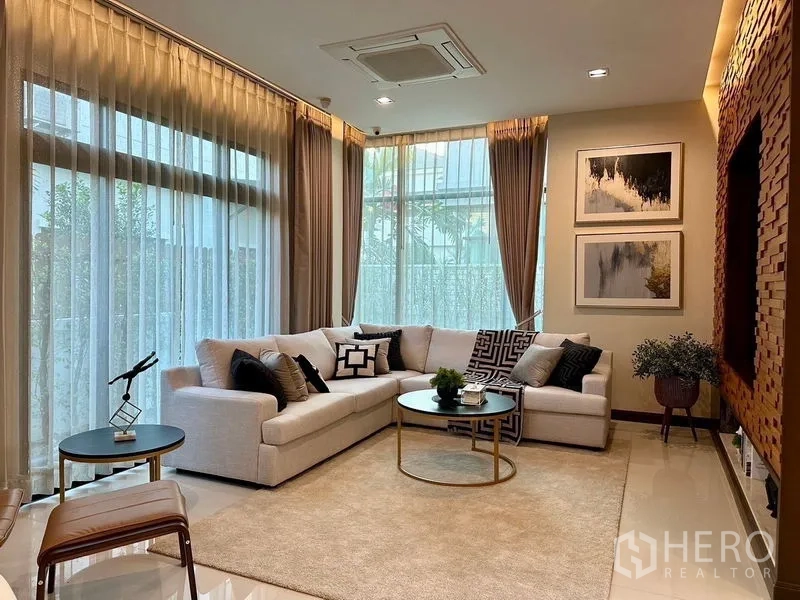 Detached House for rent - Sunlit family living room with L-shaped white sofa, large windows and neutral decor.