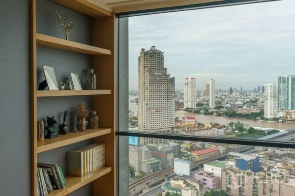公寓 出租或出售在Bang Rak, Bangkok - 内置木质书架与落地窗相邻，可俯瞰邦拉克公寓的湄南河与城市天际线。