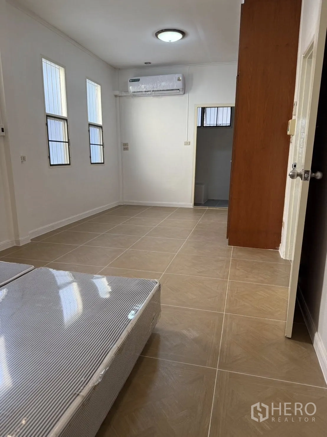 独栋房屋 for rent in Khlong Toei, Bangkok - 明亮的瓷砖房间，修长窗户、空调与通往浴室的门。