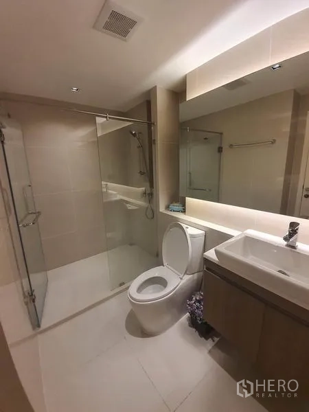 Condominium for rent in Khlong Toei, Bangkok - Contemporary bathroom with glass-enclosed shower, toilet and vanity.
