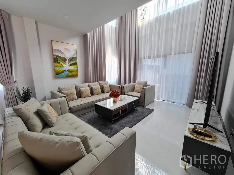 Detached House for rent or sale in Bang Phli, Samut Prakan - Double‑height living room with two sofas, sheer drapes and TV console.