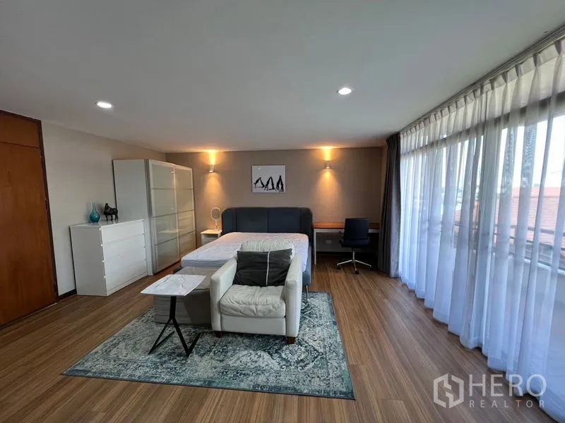 Townhouse for rent or sale in Suan Luang, Bangkok - Large corner bedroom with floor-to-ceiling windows, sheer curtains, sofa and study desk.