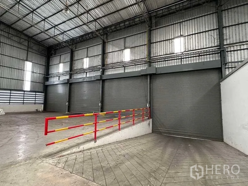Warehouse for rent in Si Racha, Chon Buri - Interior loading bay with three roller shutter doors and red safety rails.