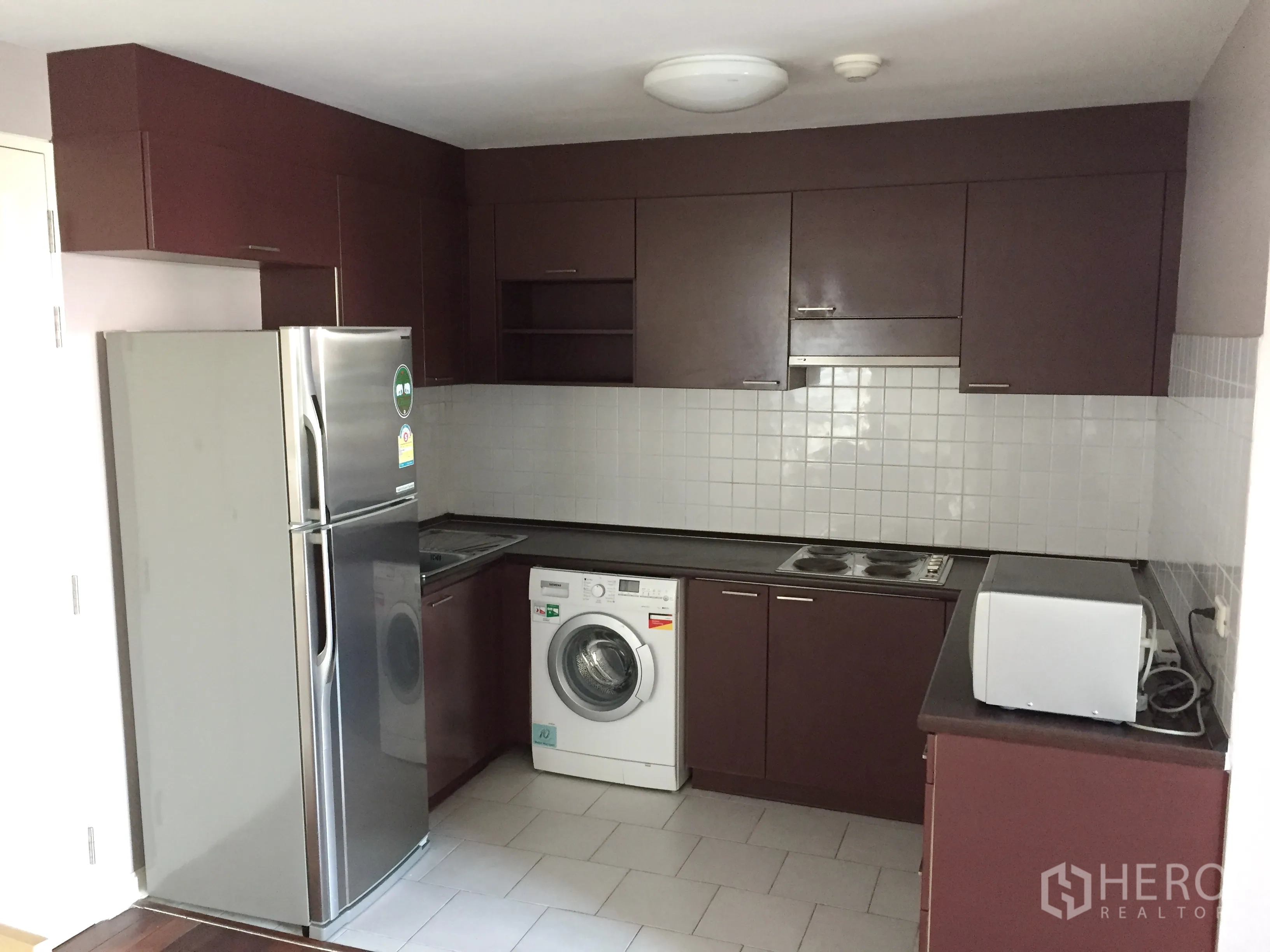 Condominium for rent in Watthana, Bangkok - Fitted kitchen with upper cabinets, cooktop, microwave, fridge and washing machine.