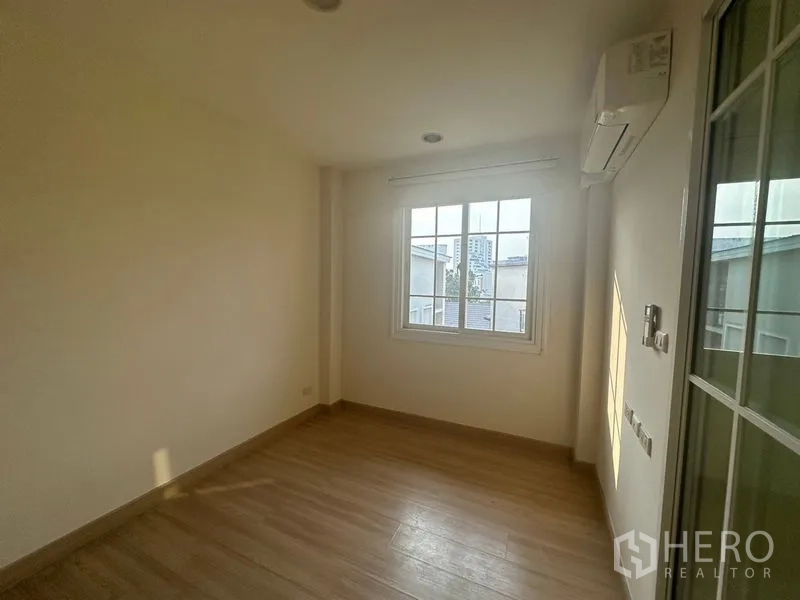 Home Office for rent in Bang Na, Bangkok - Bright empty room with wood-look flooring, window and wall-mounted air conditioner.