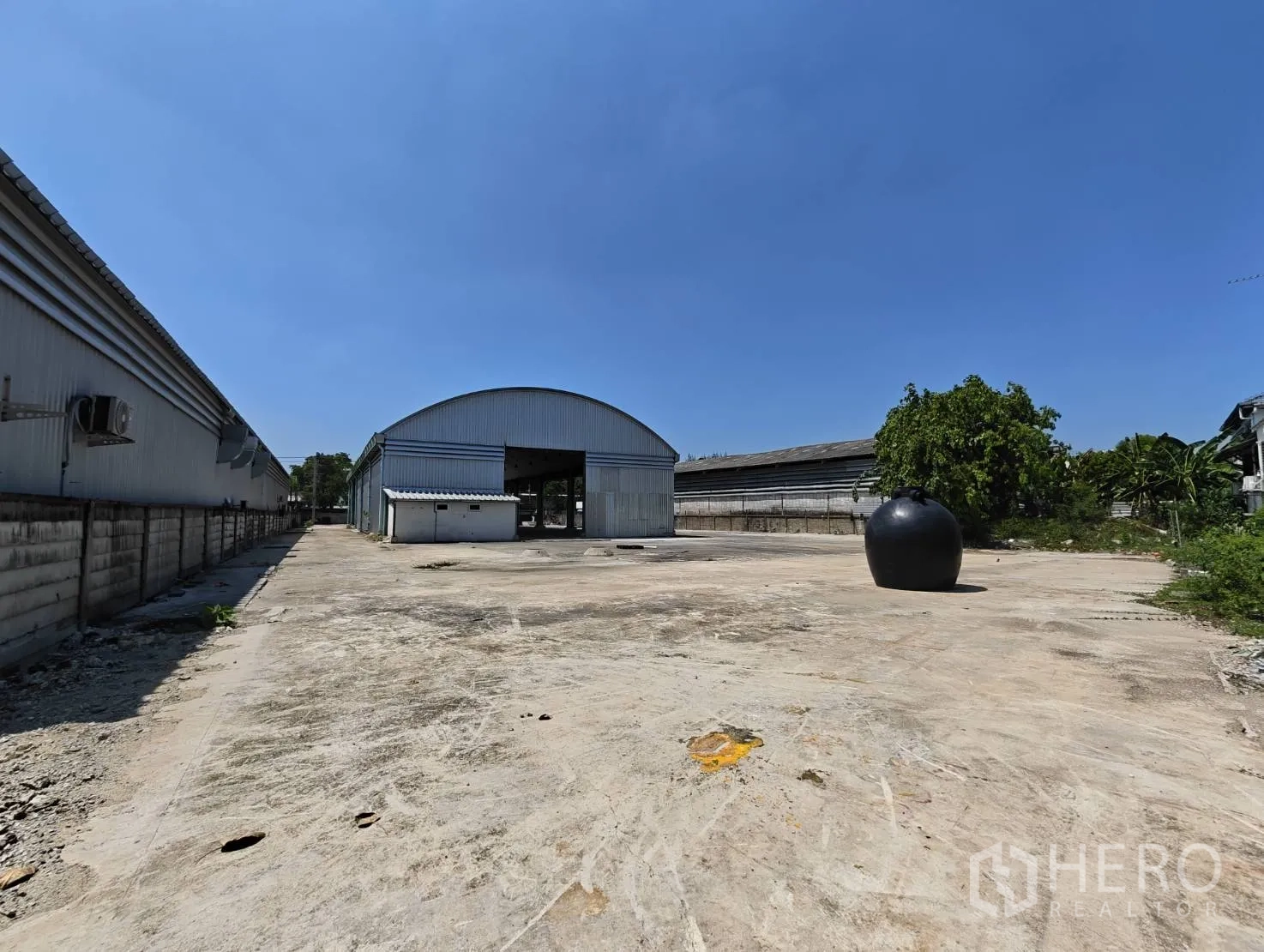 Warehouse for rent in Lak Si, Bangkok - Wide concrete yard leading to an arched metal warehouse with large entry and perimeter walls.