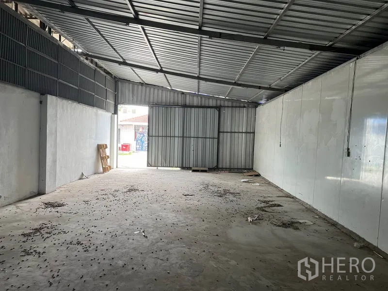 Warehouse for rent in Mueang Samut Prakan, Samut Prakan - Open-plan storage space facing a large sliding steel gate for easy truck loading.