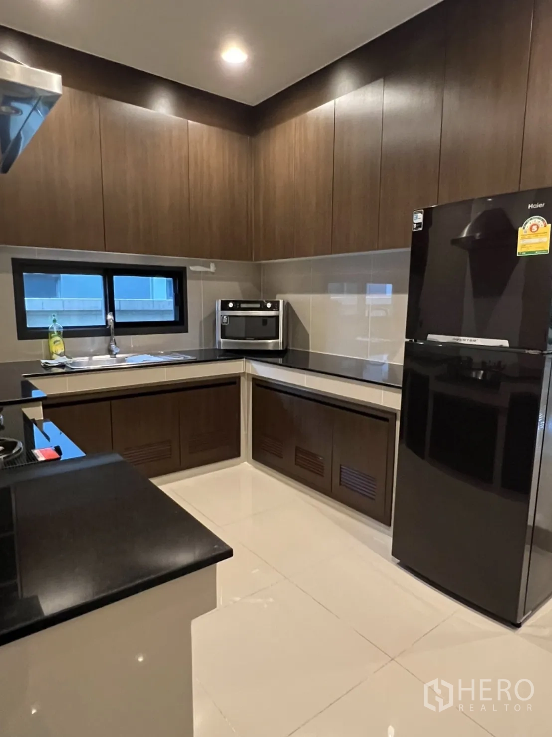 Detached House for rent or sale in Bang Kapi, Bangkok - Separate enclosed kitchen with L-shaped counters, dark cabinetry and appliances.
