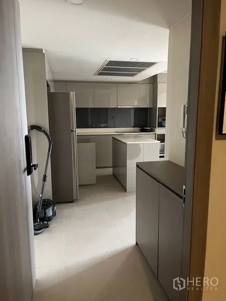 公寓 出租在Pathum Wan, Bangkok - 从门口望向的现代厨房，灰色橱柜、中岛台面与不锈钢冰箱。