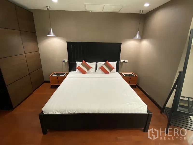 公寓 出租在Watthana, Bangkok - 主卧配深色床架与白色床品，床头吊灯与棕色墙面，木地板。
