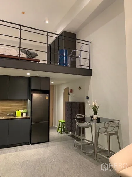 Condominium for rent in Bang Rak, Bangkok - Open kitchen with dark cabinetry beneath a mezzanine sleeping area.