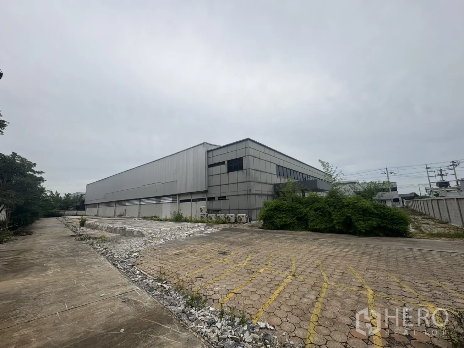 Factory for rent or sale in Samut Prakan - Long side of the warehouse with wide concrete apron and rubble area.